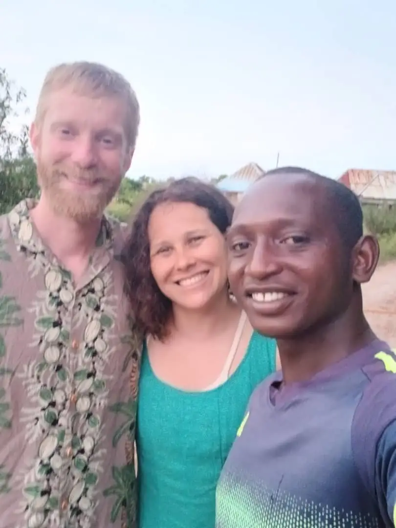 Chalii Ali standing with two guests at dusk on Pemba, all three smiling into the camera.