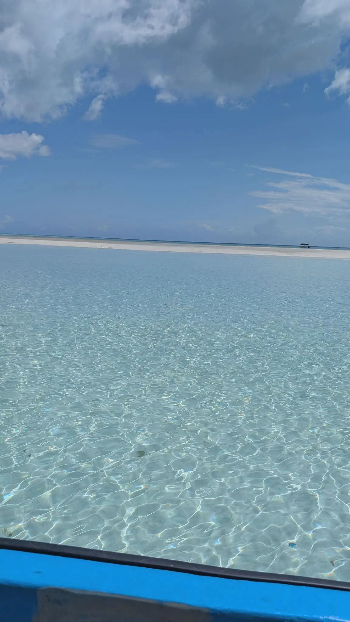 Clear shallow water over pale sand, seen over the blue gunwale of the boat.