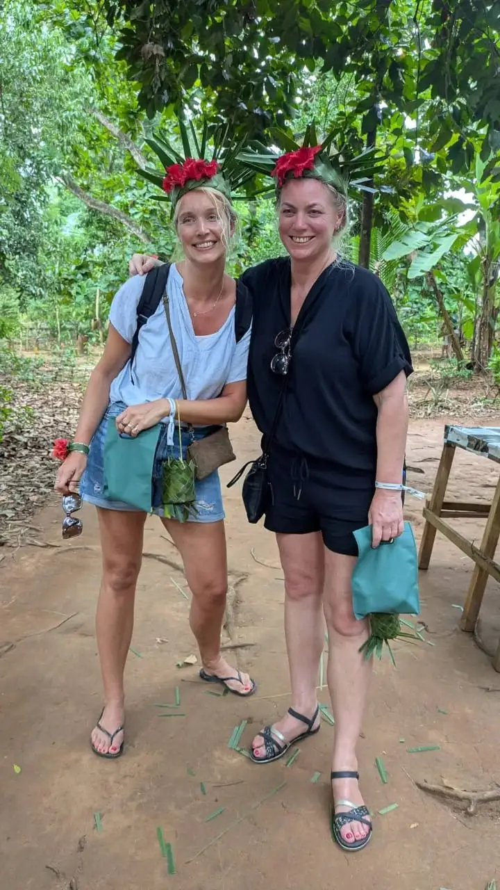 Two guests wearing crowns woven from palm leaves and red flowers by the farm guide.