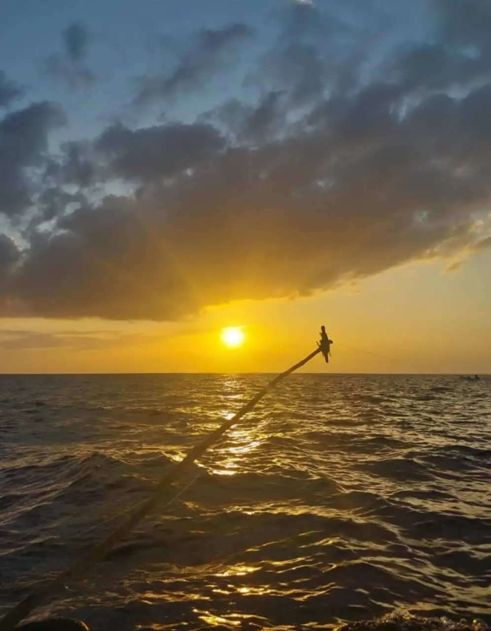 The sun dropping below a bank of cloud, seen along the dhow's rigging from on board.